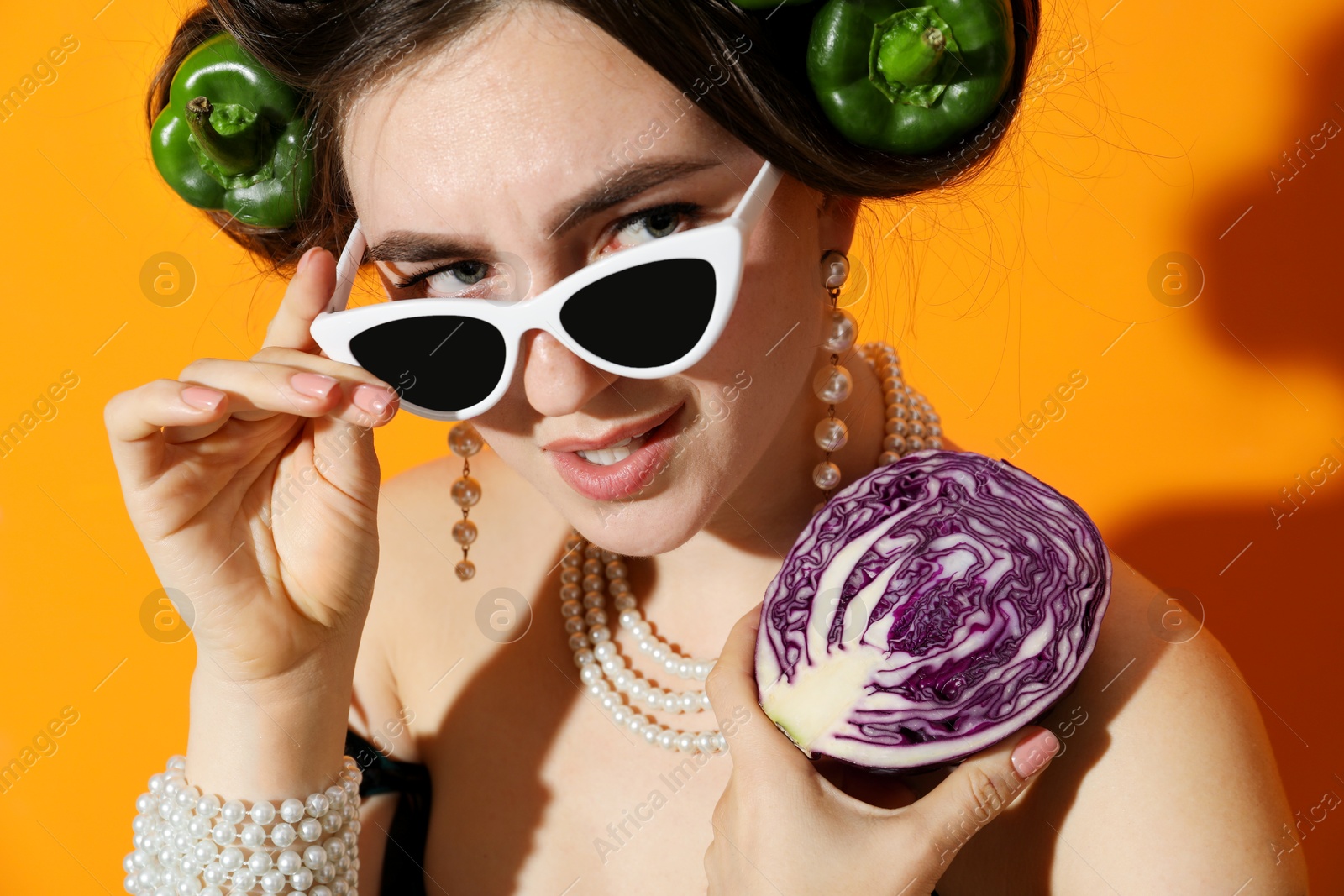 Photo of Young woman with peppers in her hair, sunglasses and red cabbage on orange background, closeup