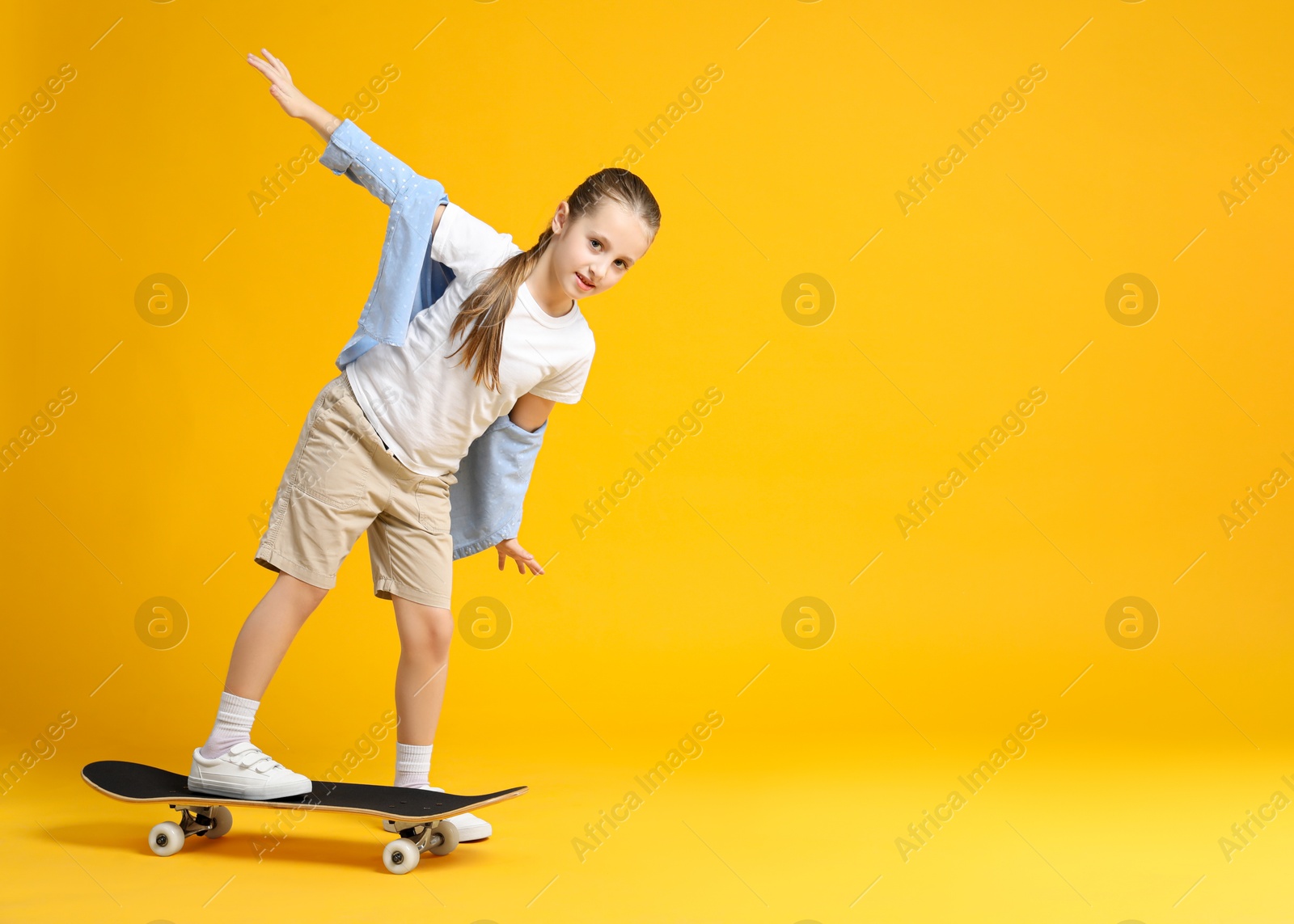 Photo of Stylish girl with skateboard on yellow background, space for text