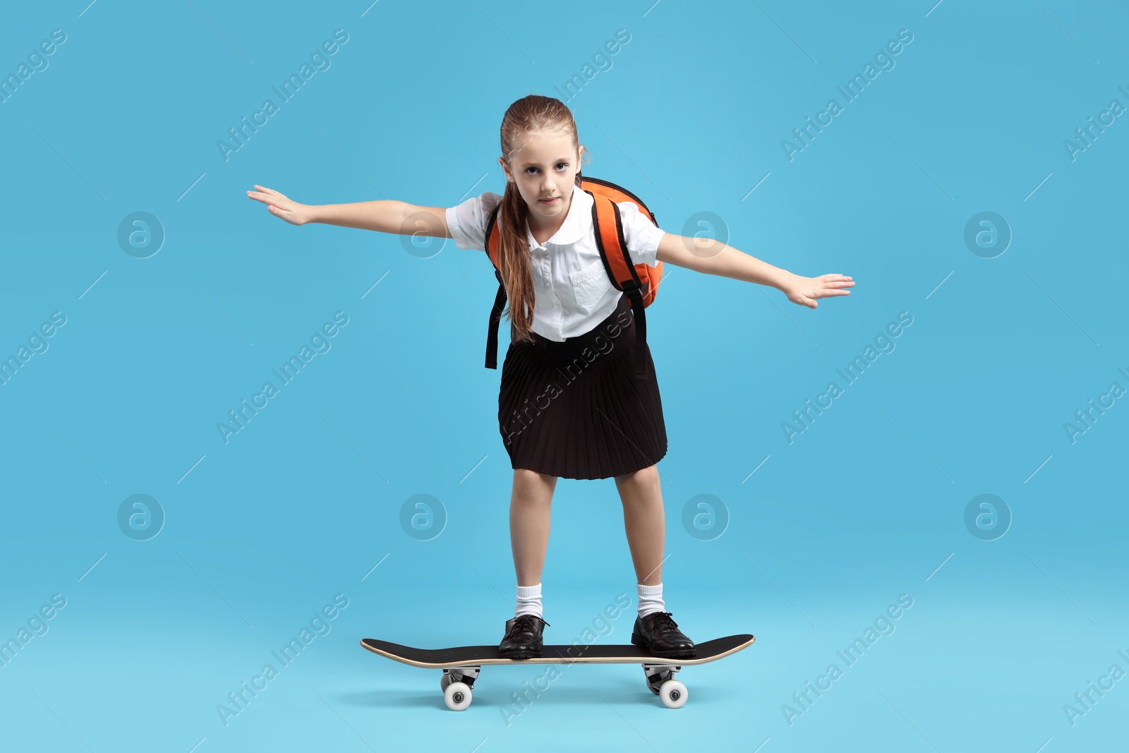 Photo of Little girl standing on skateboard against light blue background