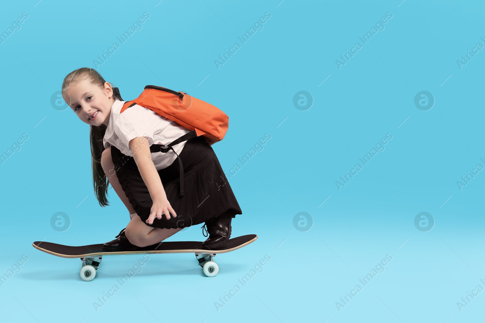 Photo of Little girl standing on skateboard against light blue background, space for text