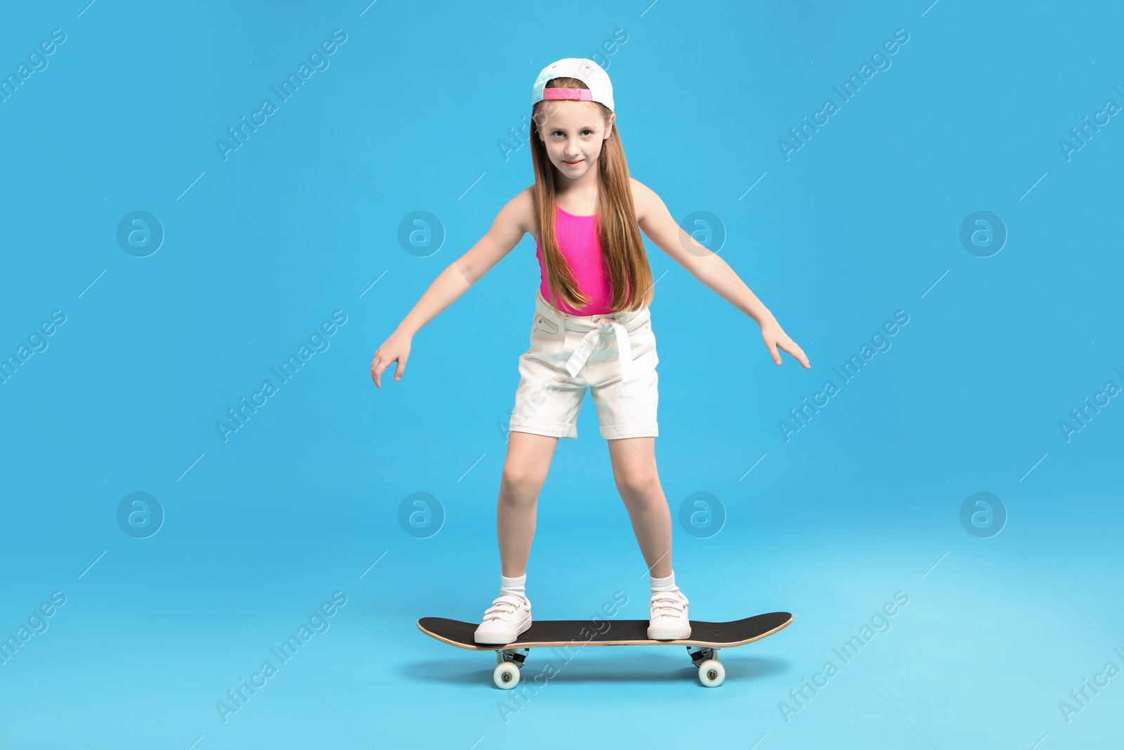 Photo of Little girl standing on skateboard against light blue background