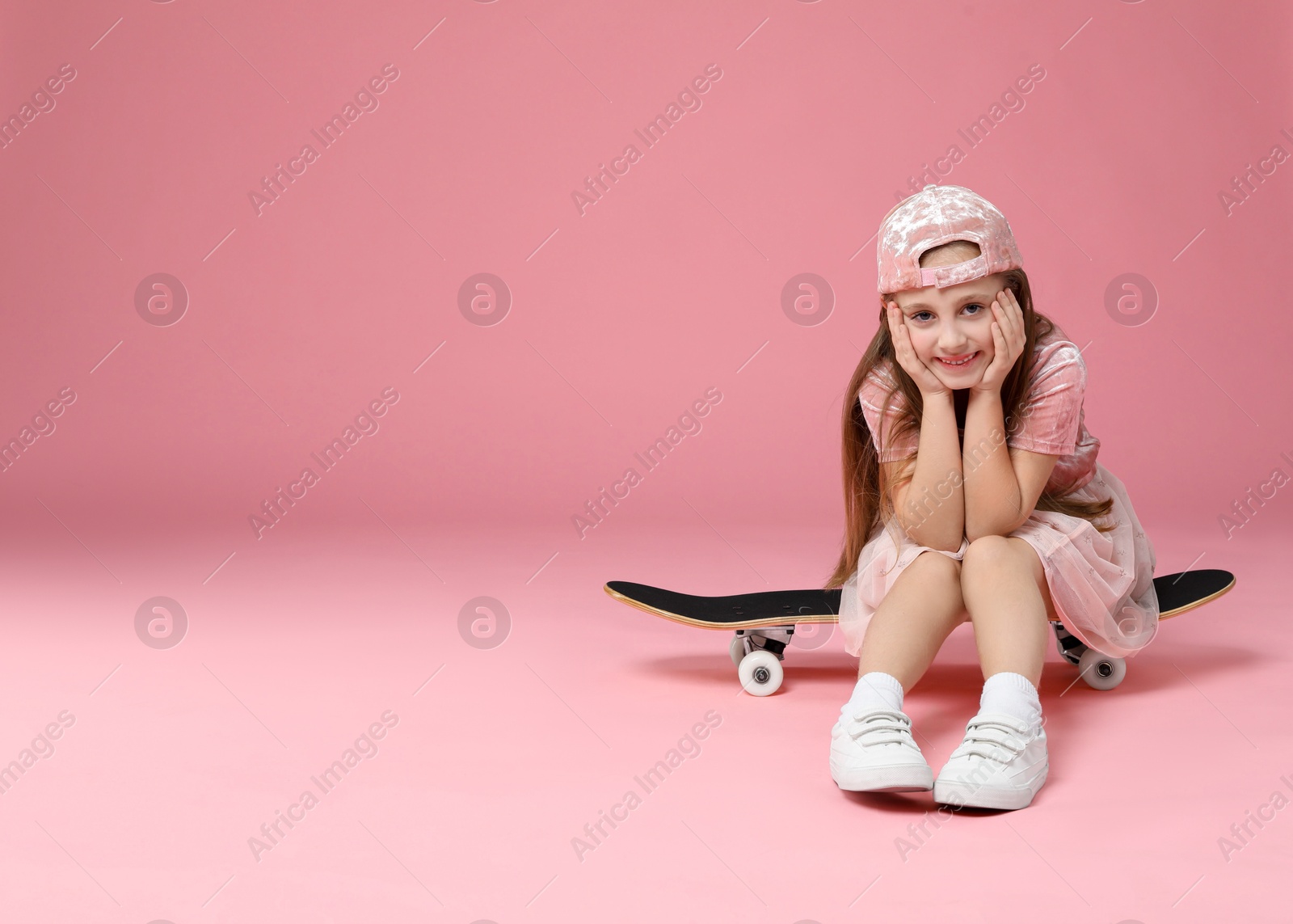 Photo of Little girl with skateboard against pink background, space for text