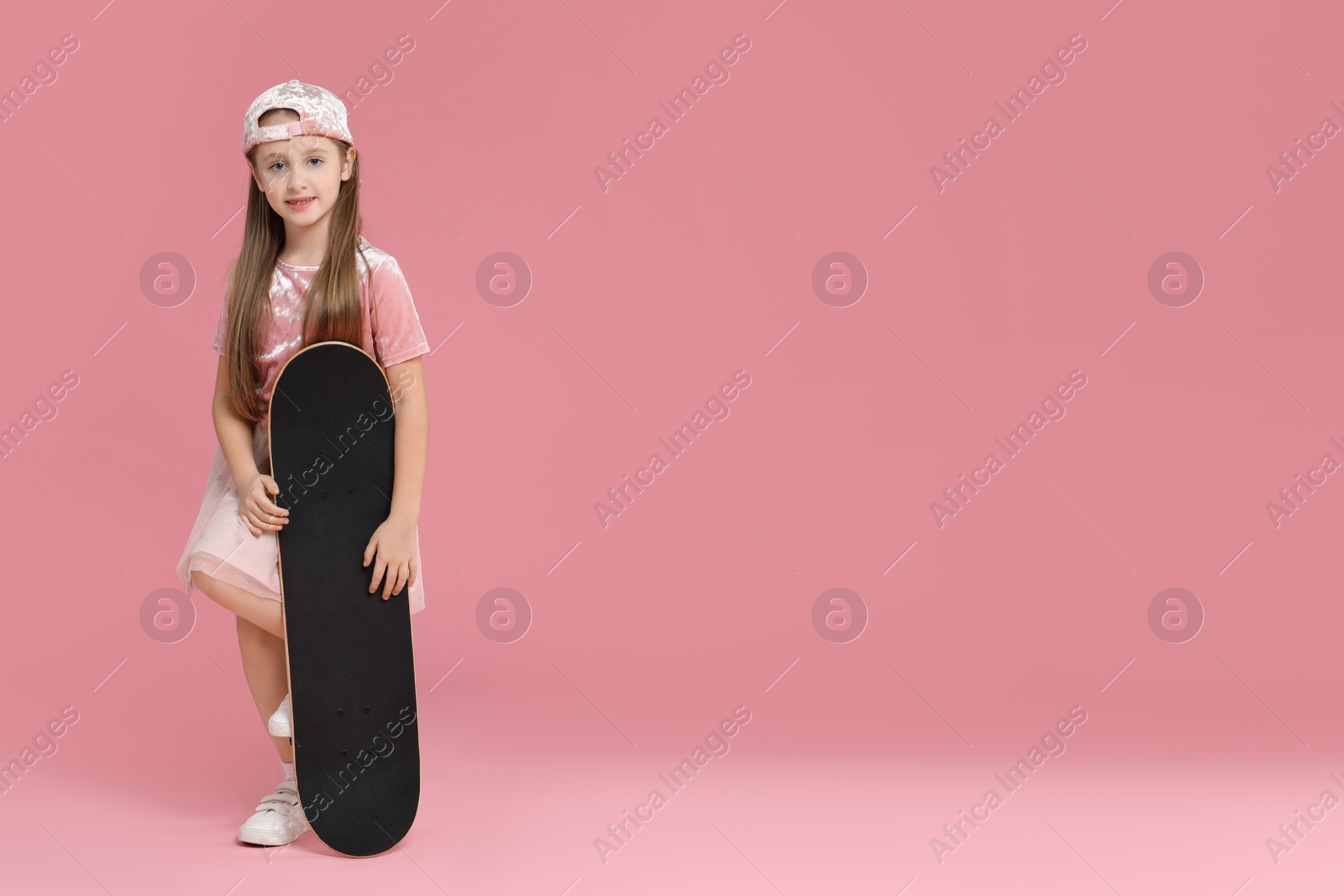 Photo of Little girl with skateboard against pink background, space for text