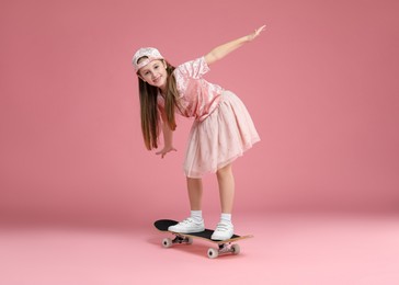 Photo of Little girl standing on skateboard against pink background. Space for text