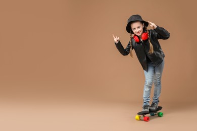 Photo of Little girl standing on penny board against pale brown background, space for text