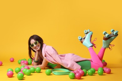 Photo of Stylish woman with retro roller skates and colorful balls on orange background