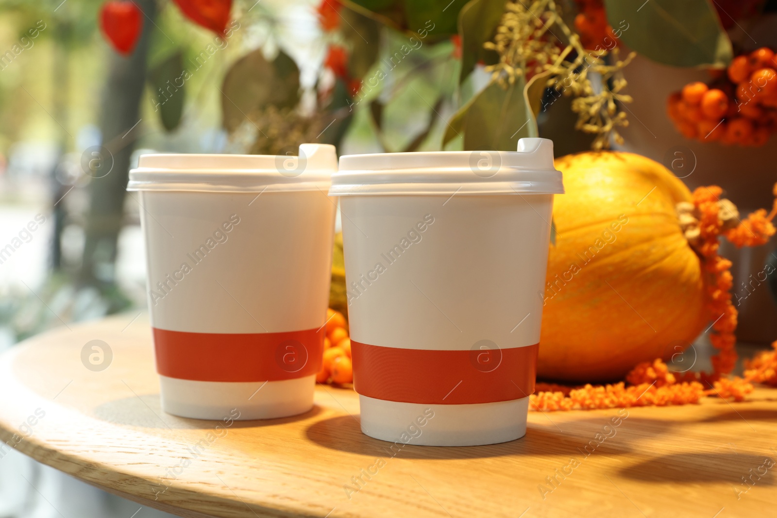 Photo of Paper cups with hot drinks and autumn decoration on wooden table in cafe