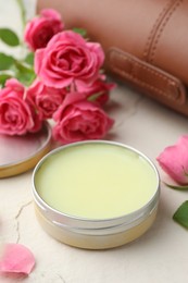 Photo of Natural solid perfume in container and pink roses on white table, closeup