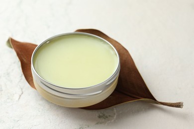 Photo of Natural solid perfume in container and dry leaf on white table, closeup