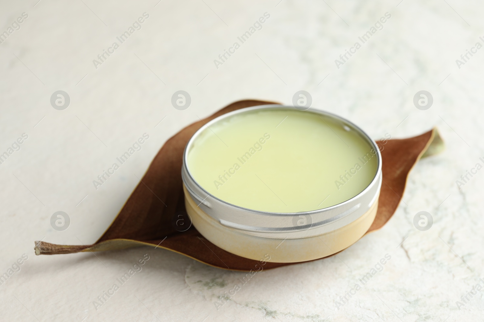 Photo of Natural solid perfume in container and dry leaf on white table, closeup