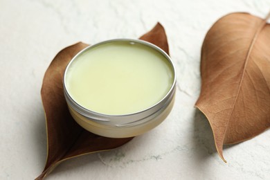 Photo of Natural solid perfume in container and dry leaves on white table, closeup