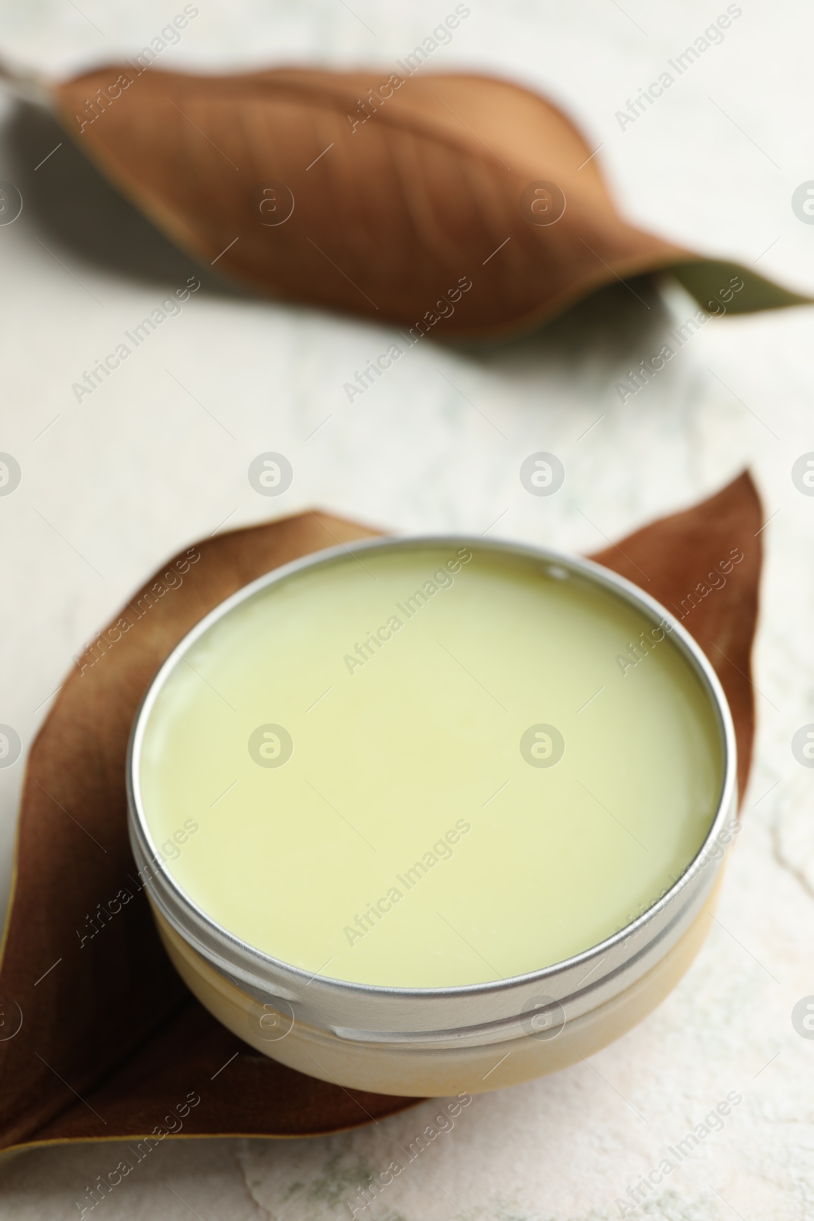 Photo of Natural solid perfume in container and dry leaves on white table, closeup