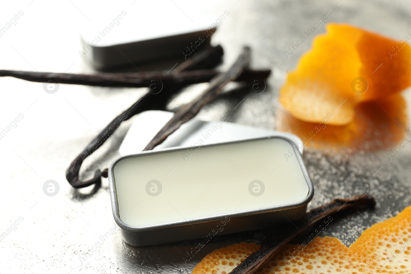 Photo of Natural solid perfume in container, vanilla pods and orange peels on grey table, closeup