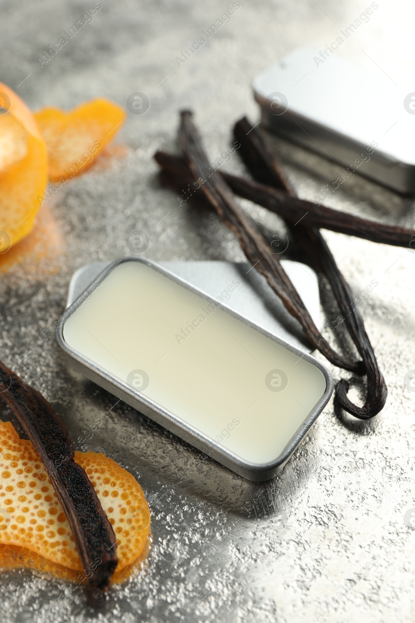 Photo of Natural solid perfume in container, vanilla pods and orange peels on grey table, closeup