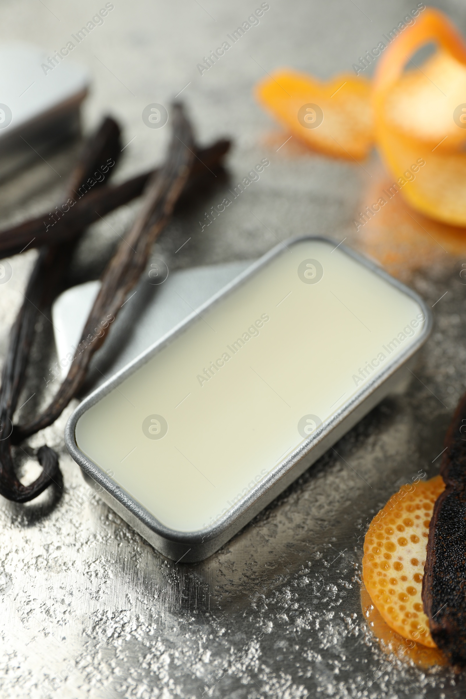 Photo of Natural solid perfume in container, vanilla pods and orange peels on grey table, closeup