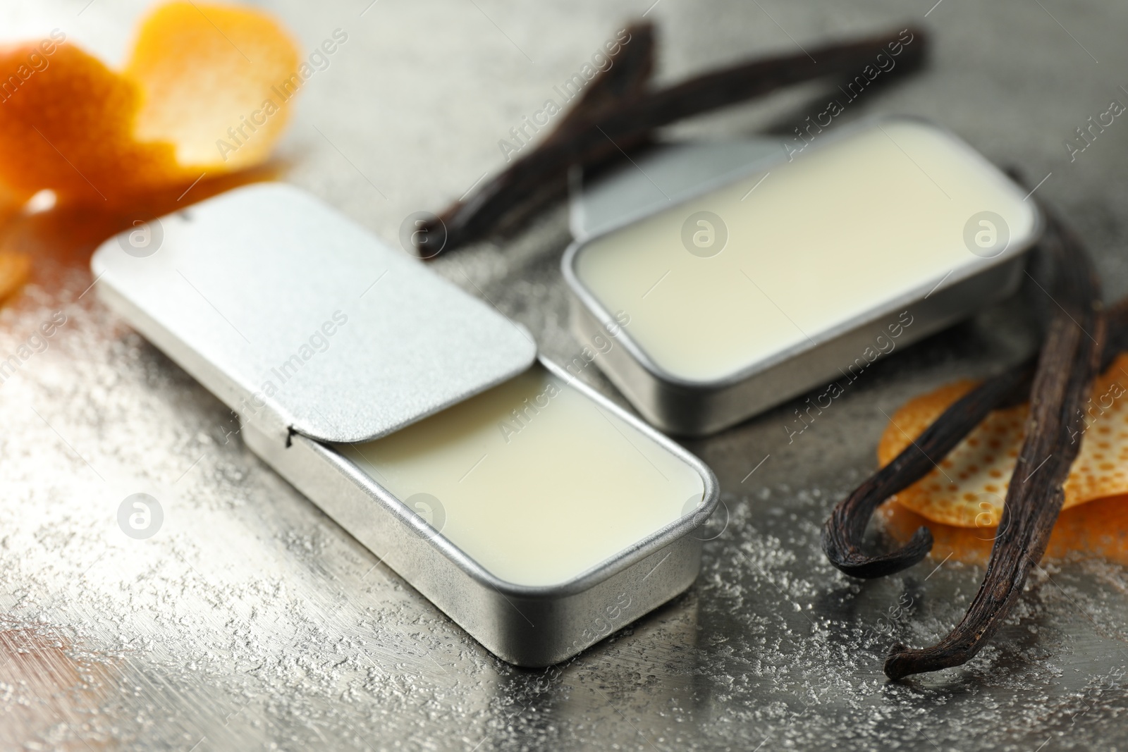 Photo of Natural solid perfume in containers, vanilla pods and orange peels on grey table, closeup