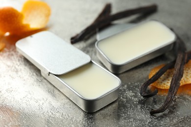 Photo of Natural solid perfume in containers, vanilla pods and orange peels on grey table, closeup