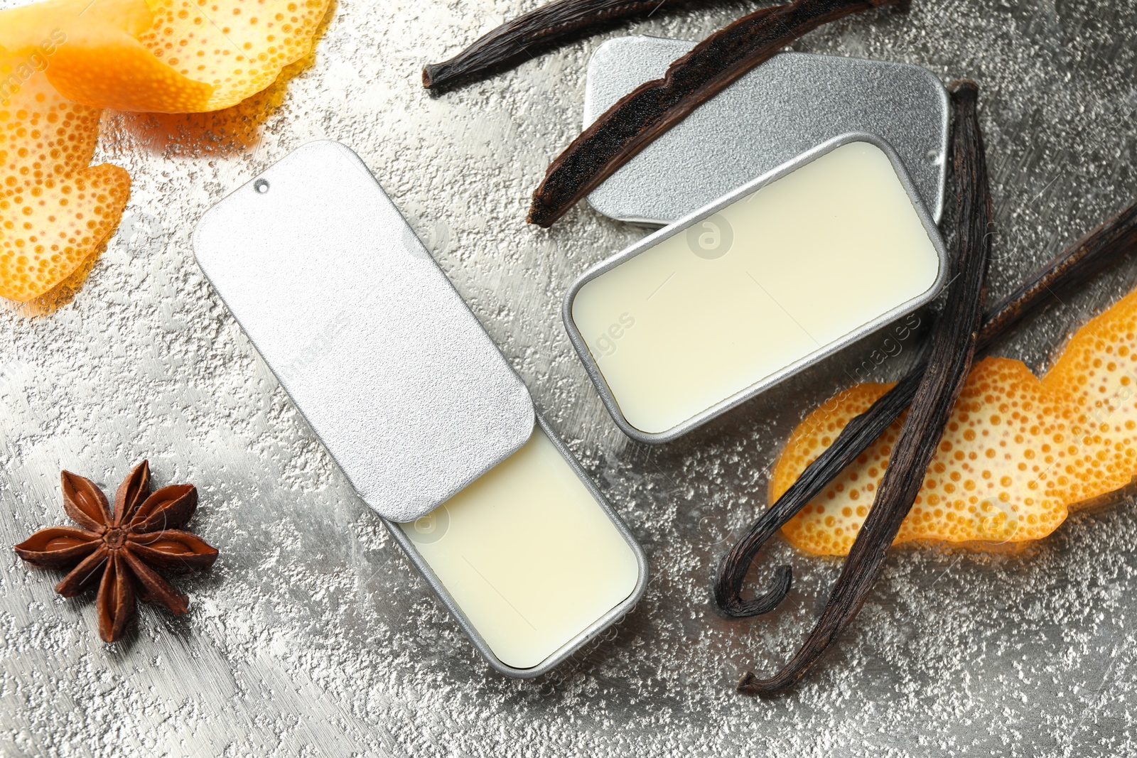 Photo of Natural solid perfume in containers, vanilla pods, anise star and orange peels on grey table, flat lay