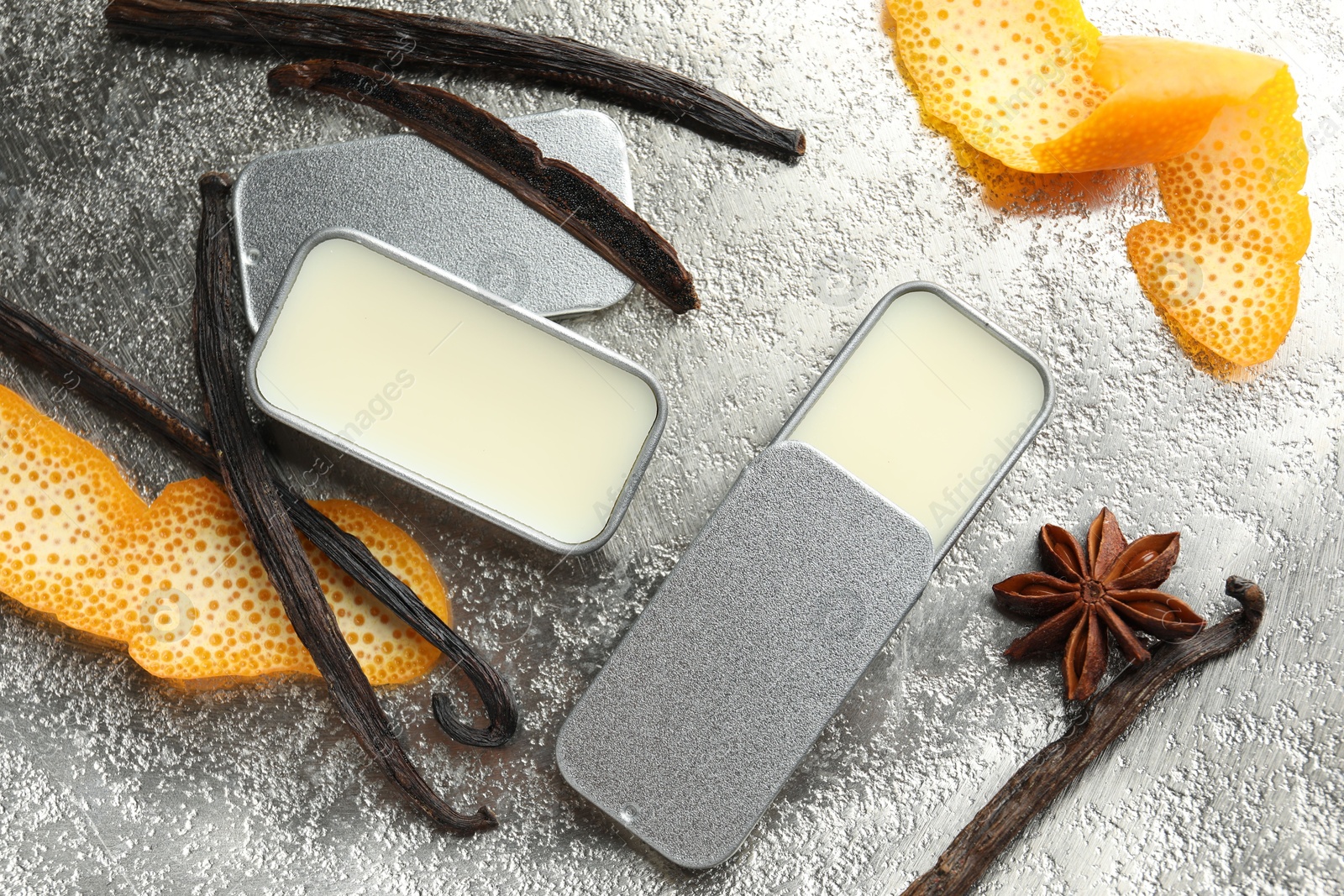 Photo of Natural solid perfume in containers, vanilla pods, anise star and orange peels on grey table, flat lay