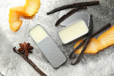 Photo of Natural solid perfume in containers, vanilla pods, anise star and orange peels on grey table, flat lay