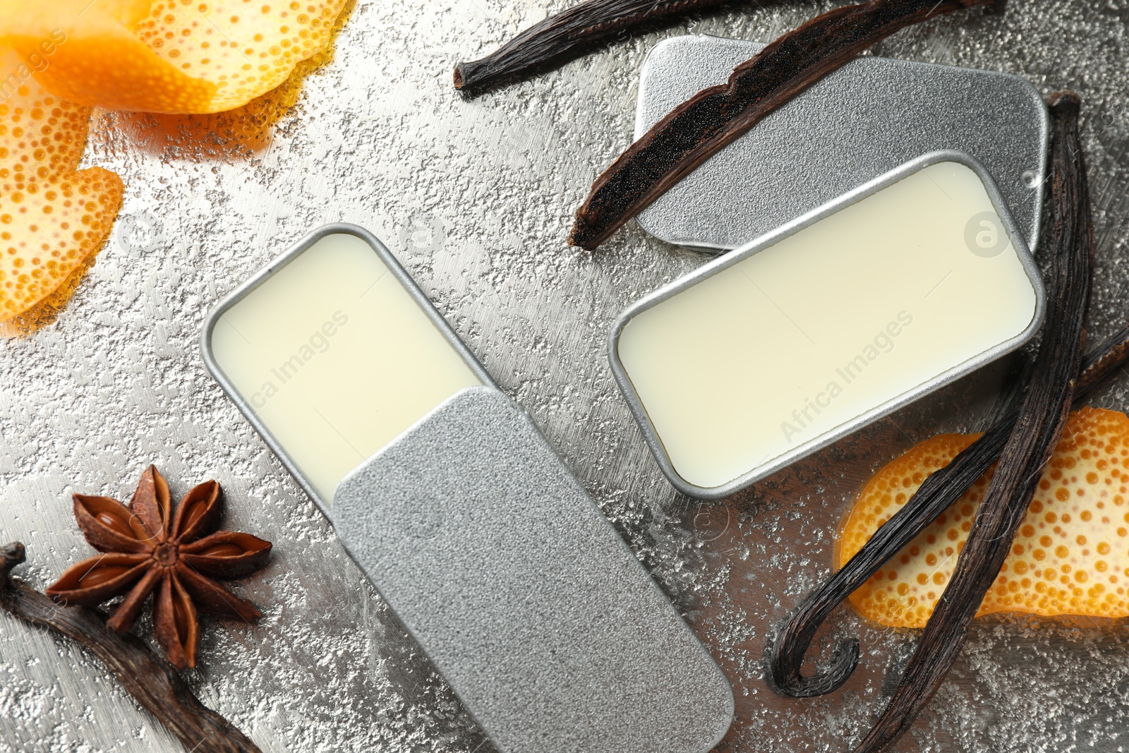 Photo of Natural solid perfume in containers, vanilla pods, anise star and orange peels on grey table, flat lay