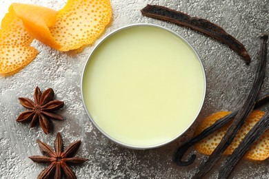 Photo of Natural solid perfume in container, vanilla pods, anise stars and orange peels on grey table, flat lay