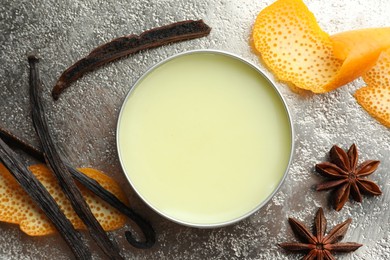 Photo of Natural solid perfume in container, vanilla pods, anise stars and orange peels on grey table, flat lay