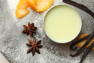 Photo of Natural solid perfume in container, vanilla pods, anise stars and orange peels on grey table, flat lay