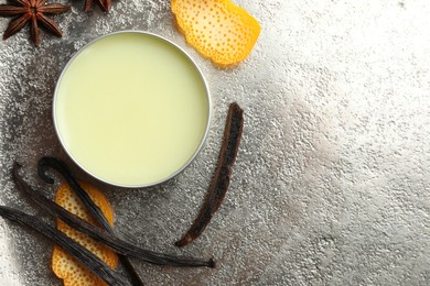 Photo of Natural solid perfume in container, vanilla pods, anise and orange peels on grey table, flat lay. Space for text