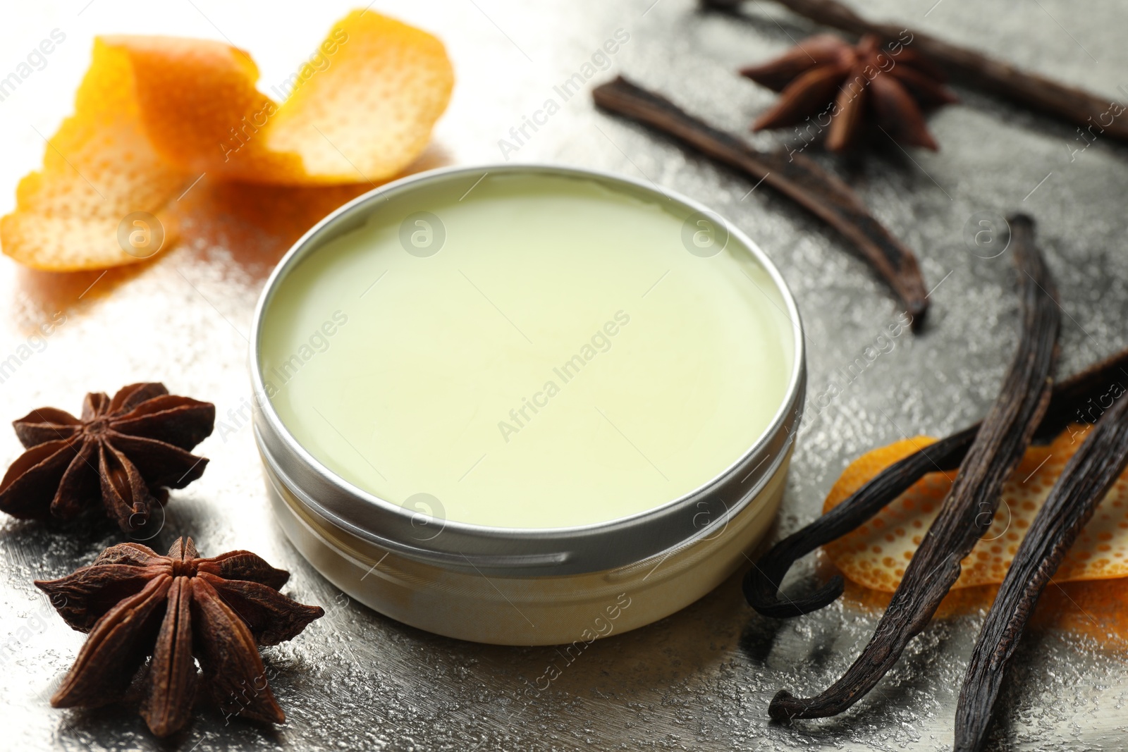 Photo of Natural solid perfume in container, vanilla pods, anise stars and orange peels on grey table, closeup