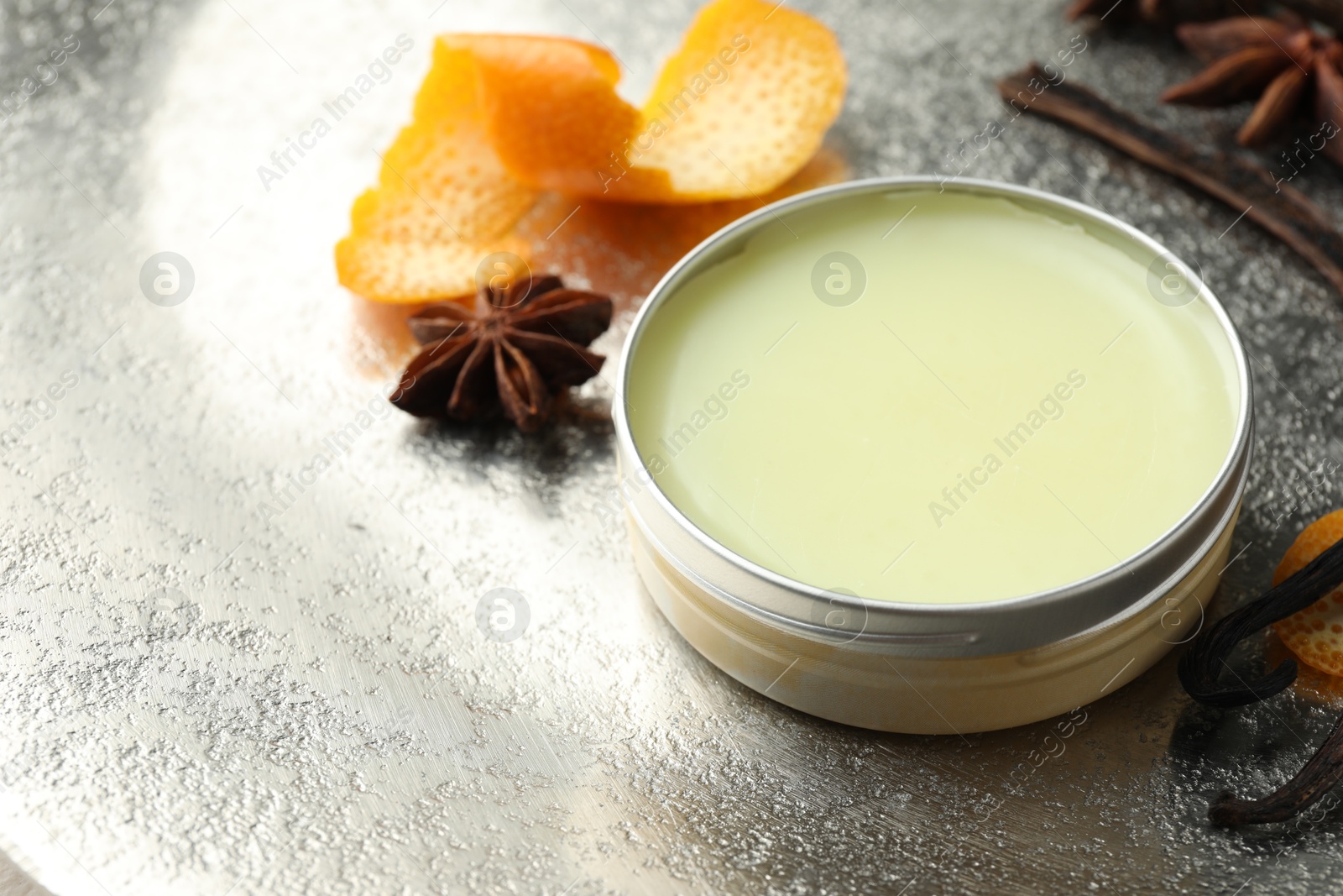 Photo of Natural solid perfume in container, vanilla pods, anise stars and orange peels on grey table, closeup. Space for text