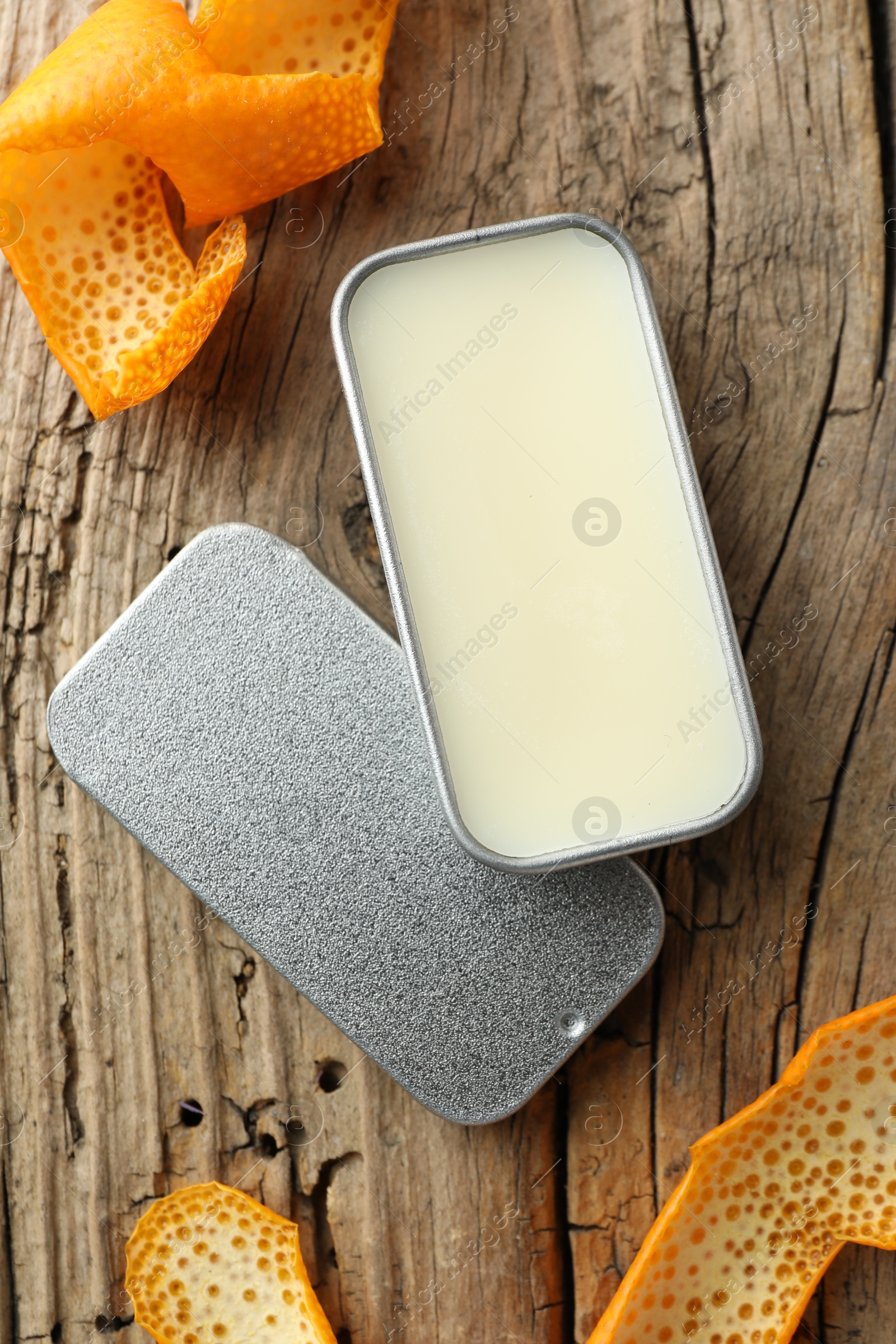 Photo of Natural solid perfume in container and orange peels on wooden table, flat lay