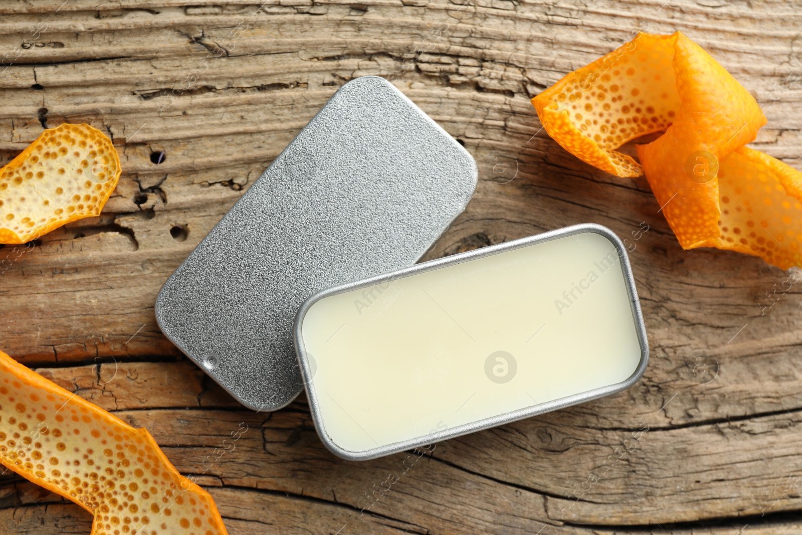 Photo of Natural solid perfume in container and orange peels on wooden table, flat lay