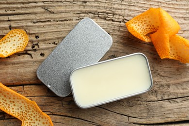 Photo of Natural solid perfume in container and orange peels on wooden table, flat lay