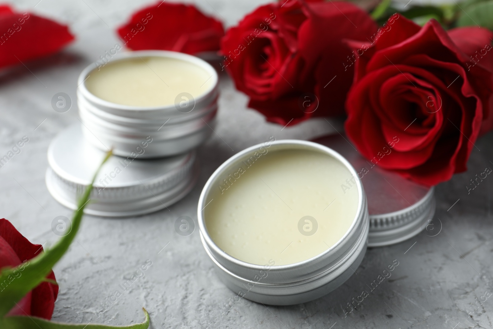 Photo of Natural solid perfume in containers and roses on grey table, closeup