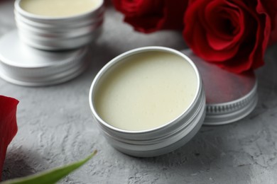 Photo of Natural solid perfume in containers and roses on grey table, closeup