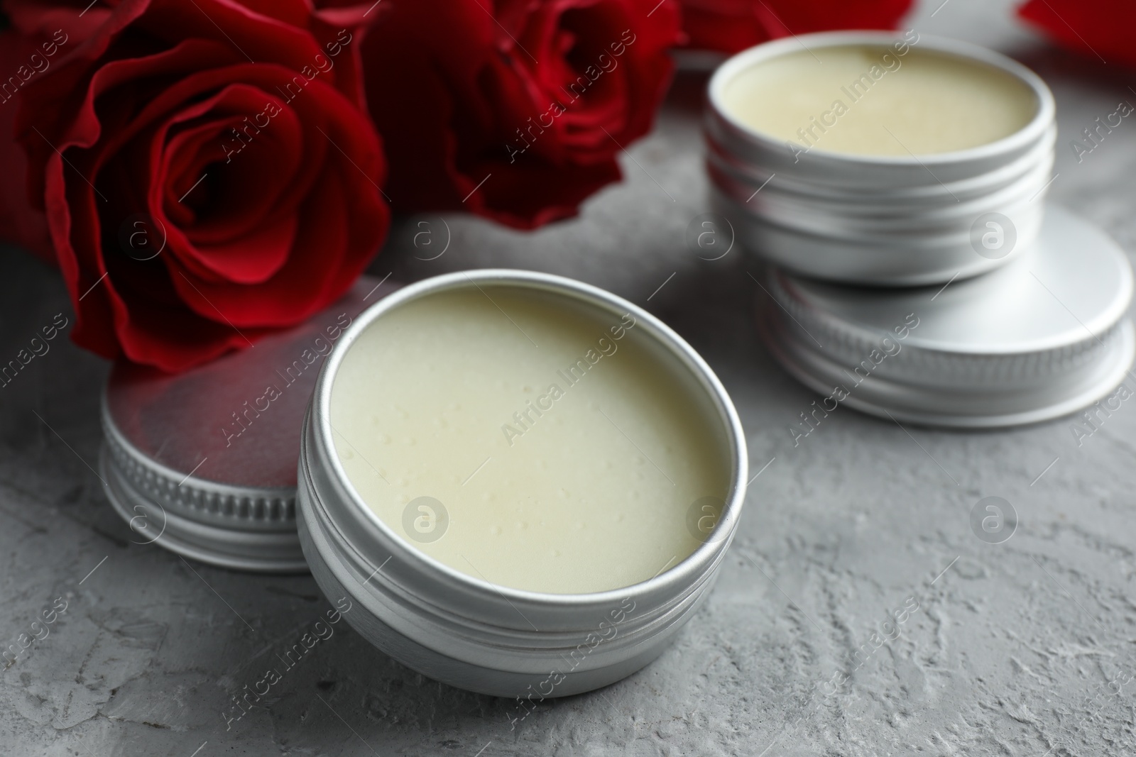 Photo of Natural solid perfume in containers and roses on grey table, closeup