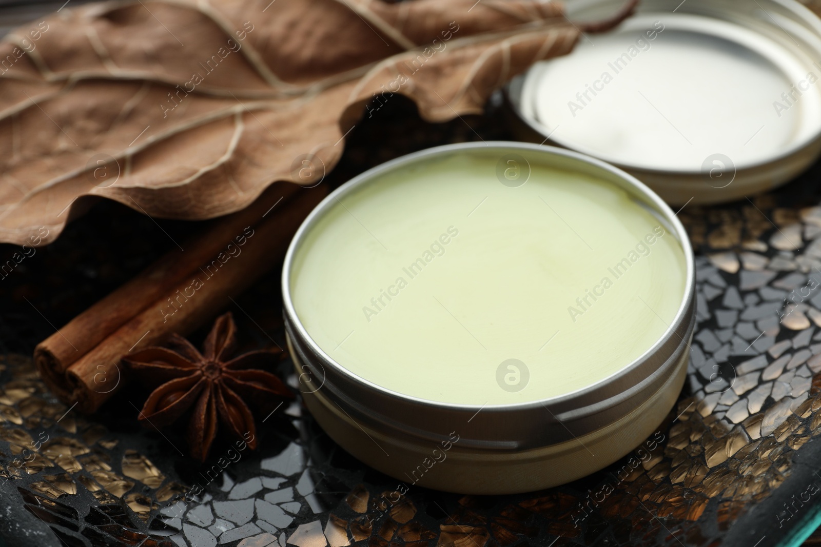 Photo of Natural solid perfume in container, spices and dry leaf on surface, closeup