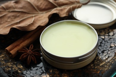 Photo of Natural solid perfume in container, spices and dry leaf on surface, closeup