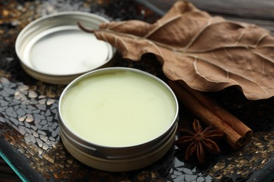 Photo of Natural solid perfume in container, spices and dry leaf on surface, closeup