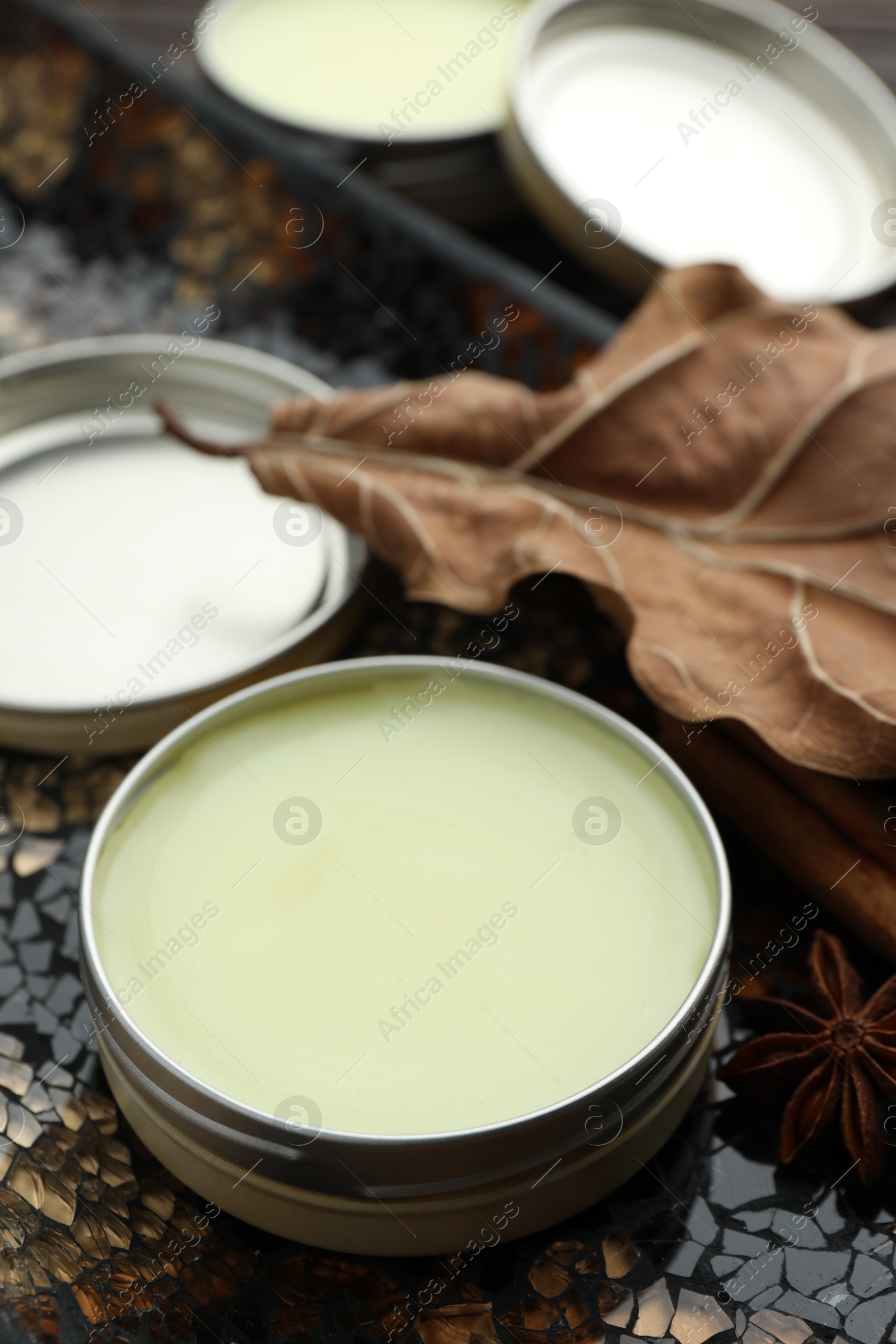 Photo of Natural solid perfume in container, spices and dry leaf on surface, closeup