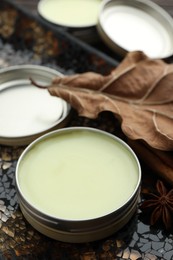 Photo of Natural solid perfume in container, spices and dry leaf on surface, closeup