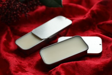 Photo of Natural solid perfume in containers on red fabric, closeup