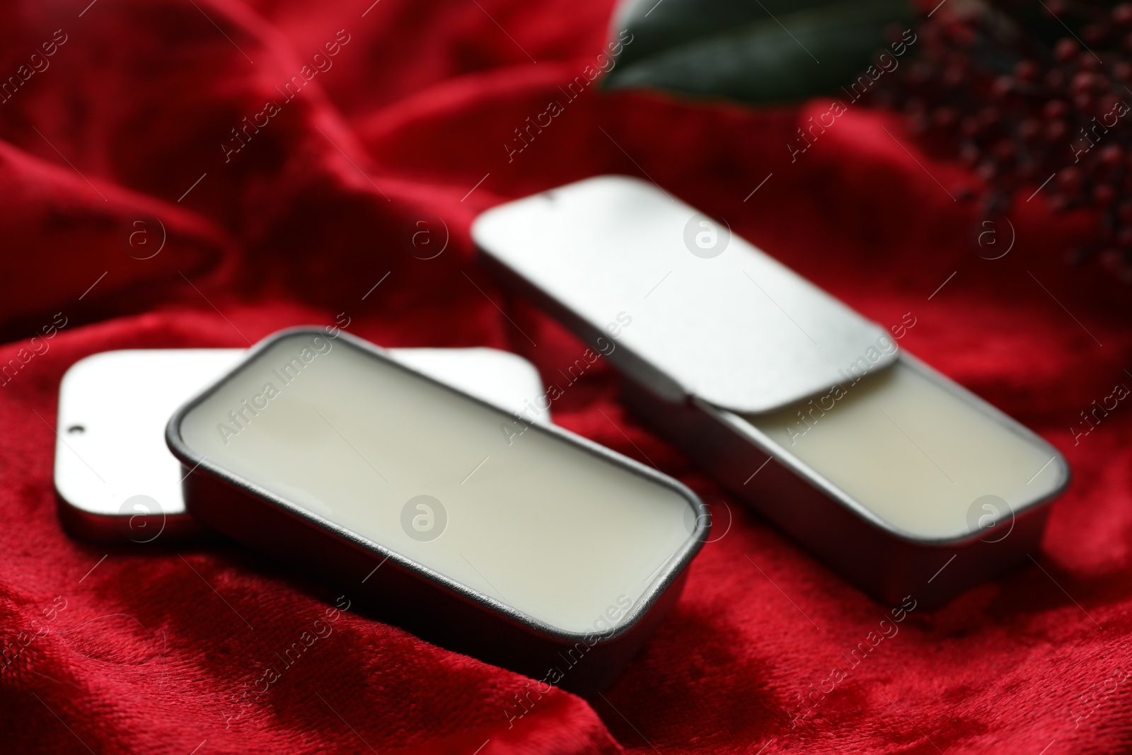 Photo of Natural solid perfume in containers on red fabric, closeup