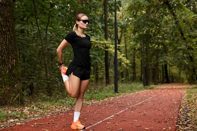 Photo of Young athletic woman stretching in park, space for text