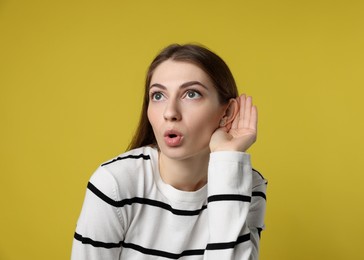 Photo of Woman showing hand to ear gesture on dark yellow background