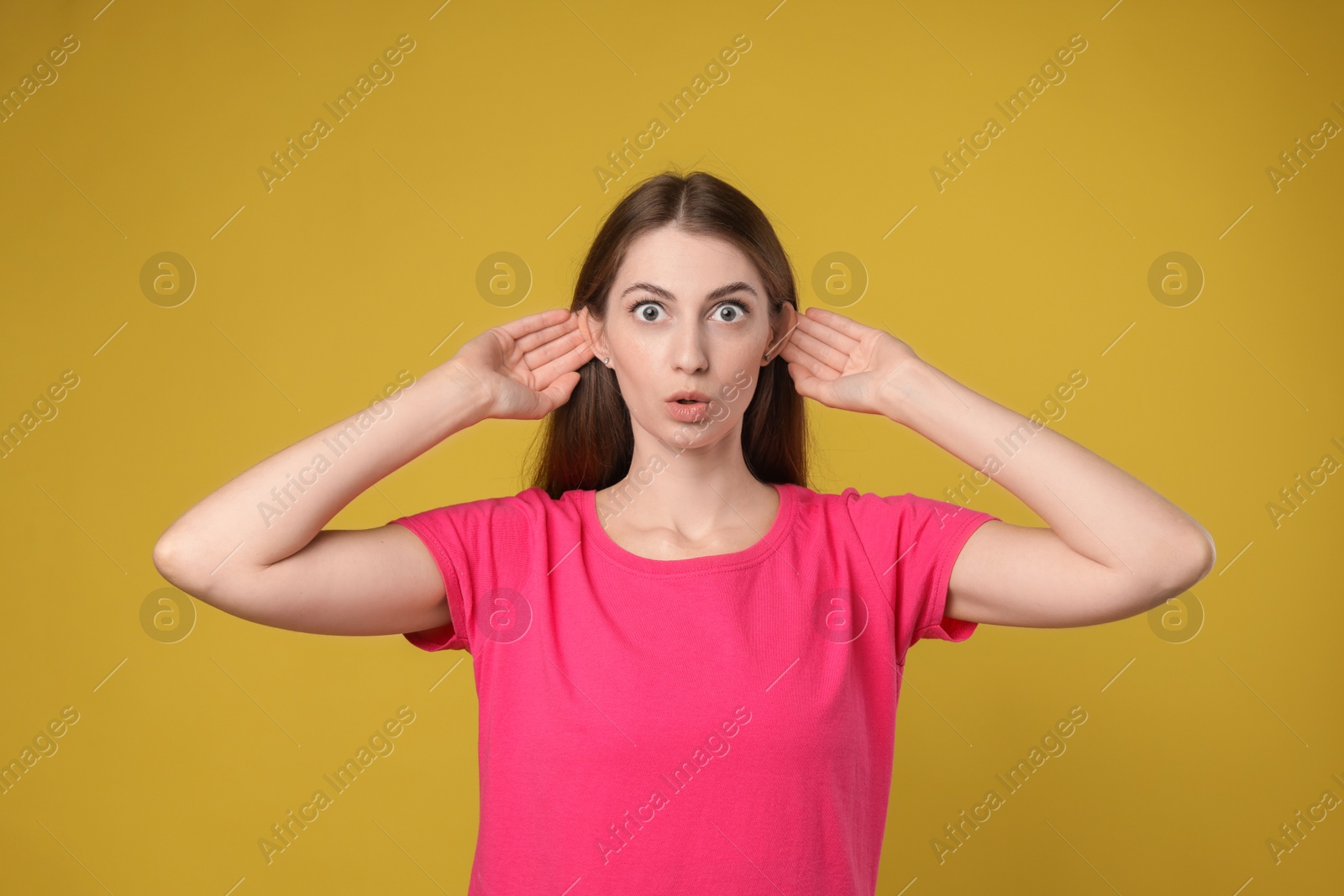 Photo of Woman showing hand to ear gesture on dark yellow background