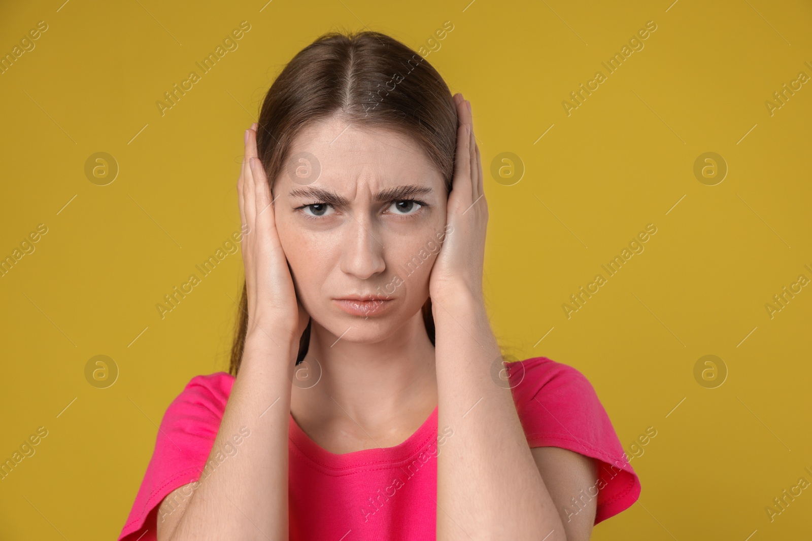 Photo of Woman covering her ears on dark yellow background