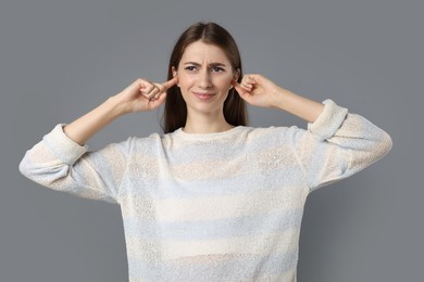 Photo of Woman covering her ears with fingers on grey background