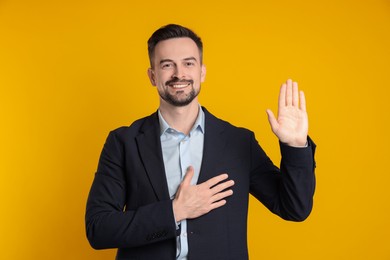 Man making promise with raised hand on orange background. Oath gesture